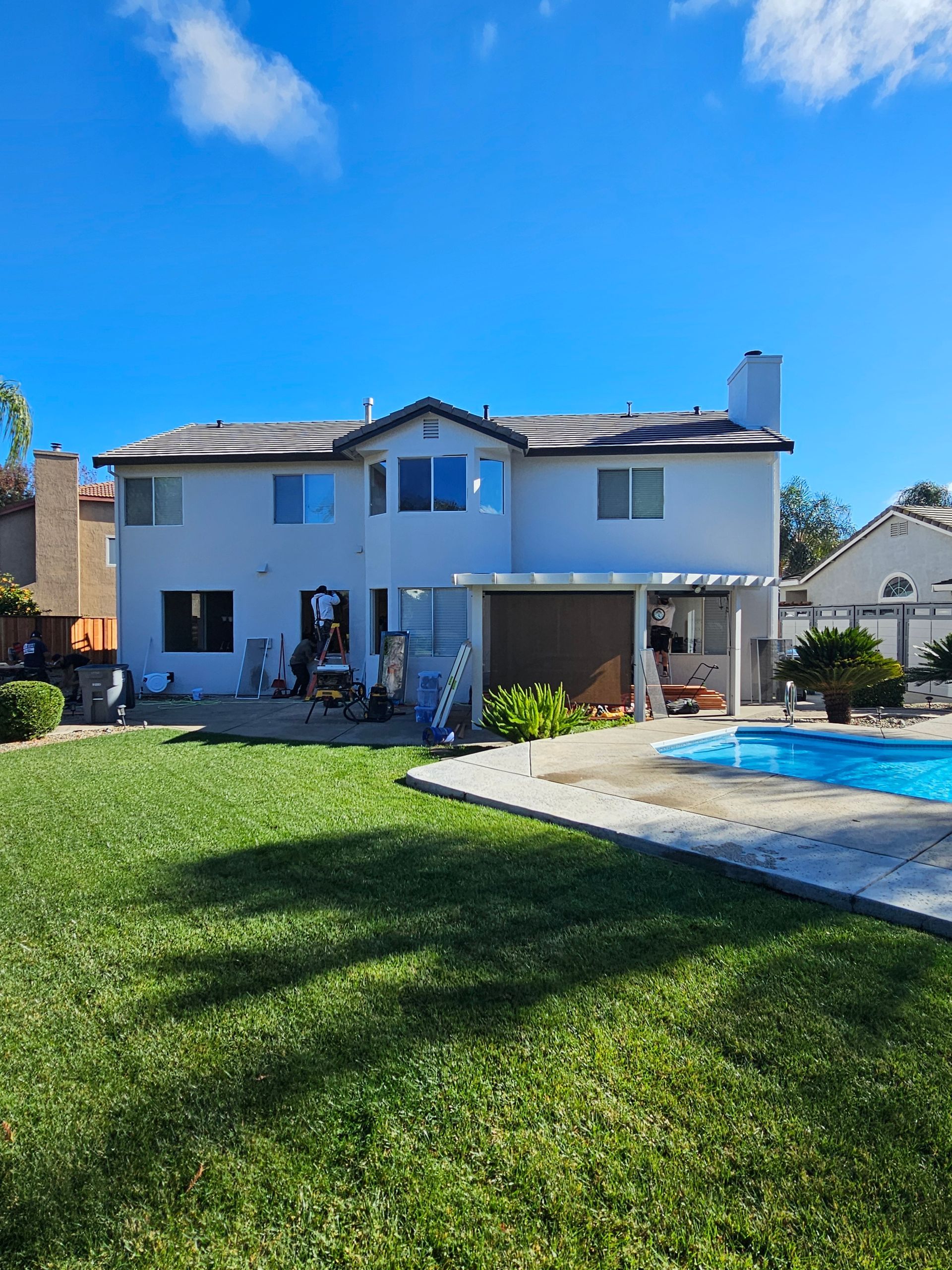Two-story white house with a backyard lawn and swimming pool under a bright blue sky