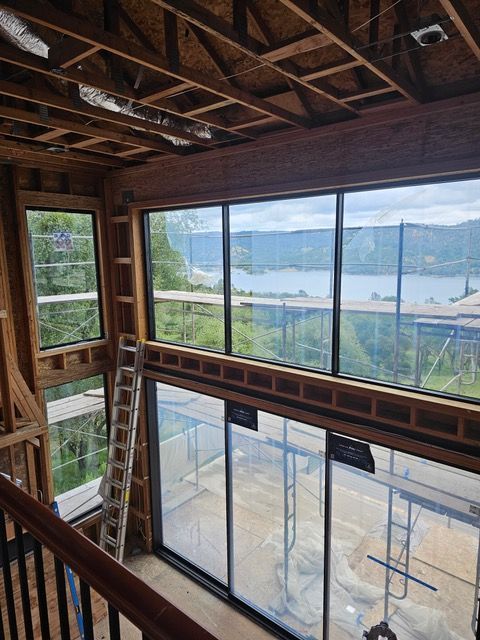 Interior of unfinished room with exposed beams and large windows overlooking a river and bridge