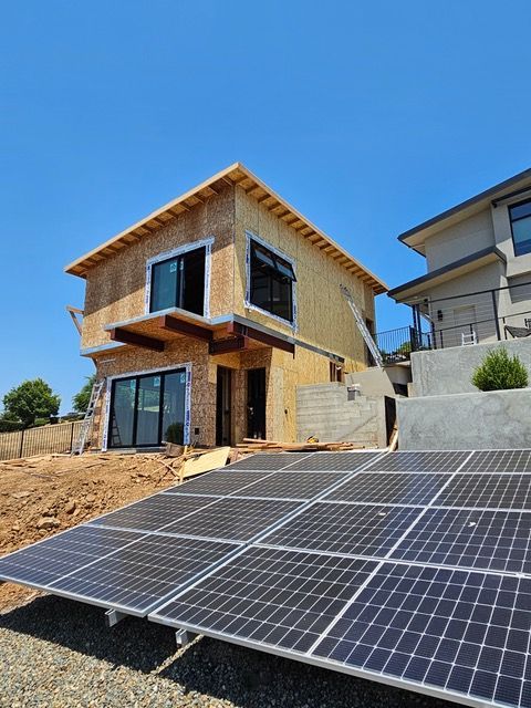 Two-story house under construction with rooftop solar panels in a sunny, dry lot