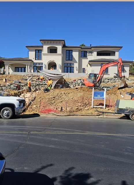 Construction site with excavator in front of a large unfinished house on a hillside