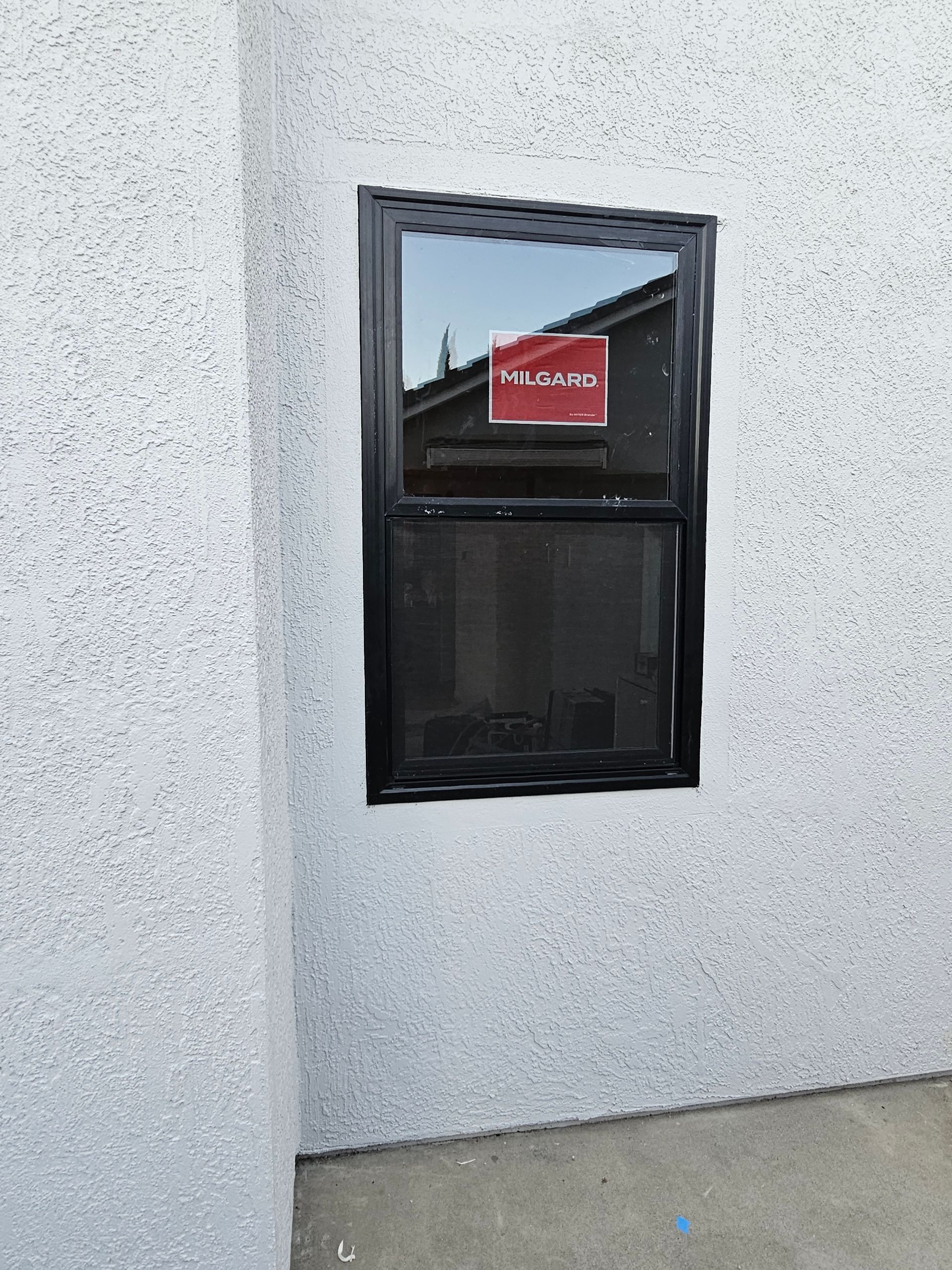 White stucco wall with a small black window and a red sign visible in the reflection