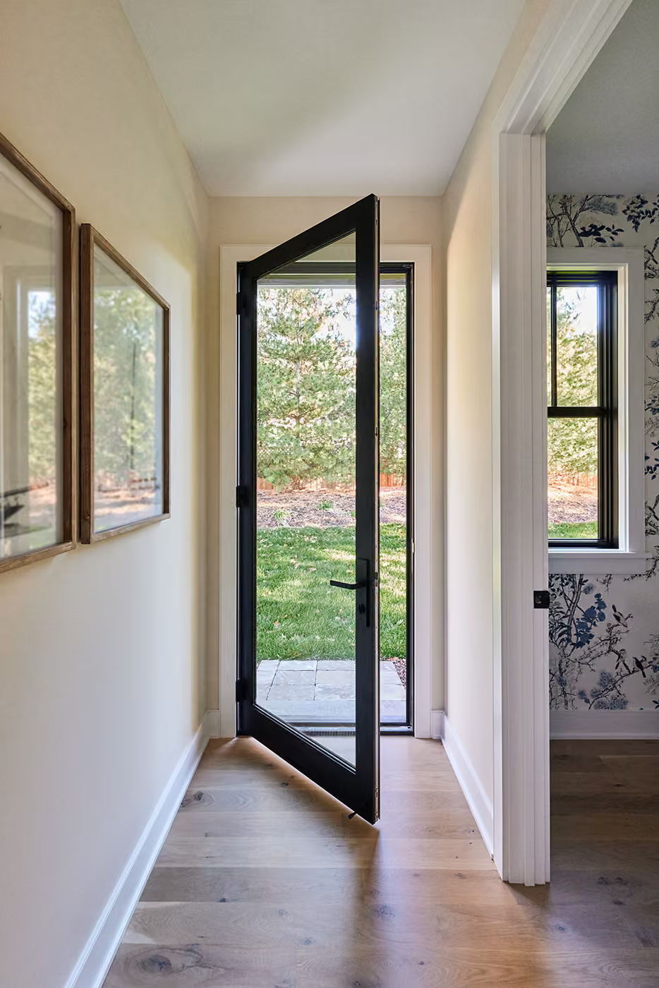 Open front door in a narrow hallway with windows and a view of a garden.