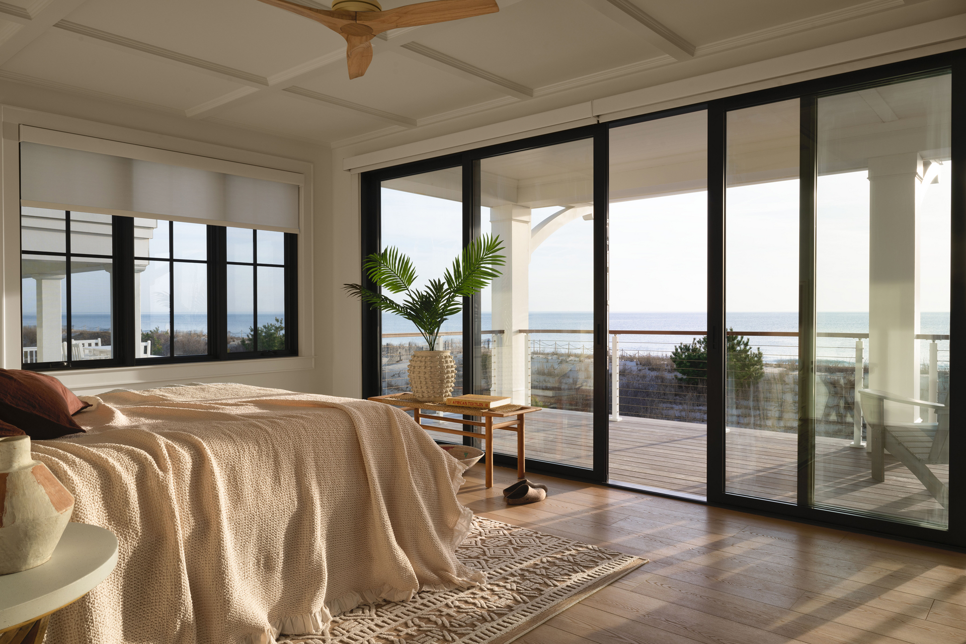 Bright bedroom with bed, woven rug, and sliding glass doors opening to a seaside balcony.
