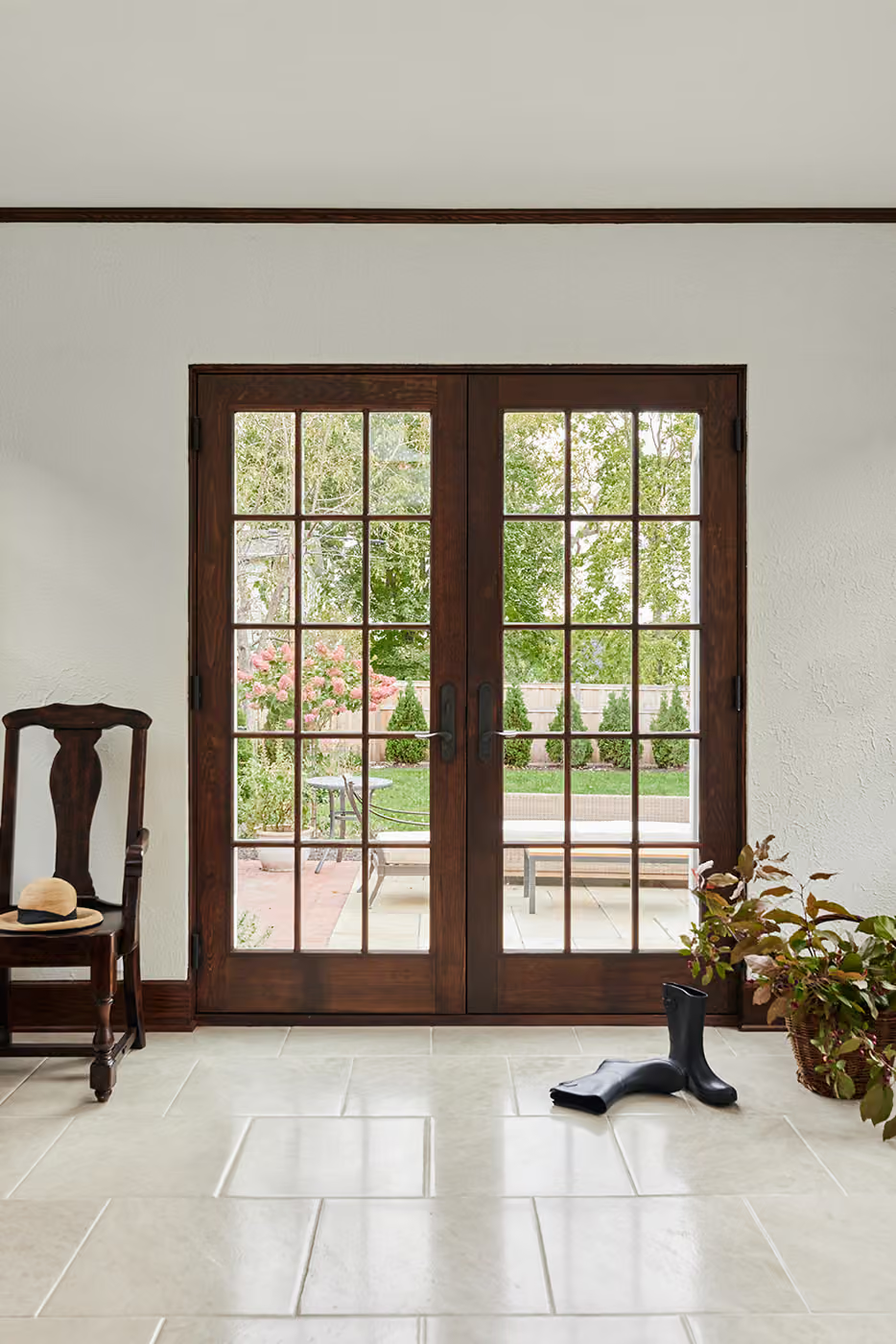 Bright room with wooden French doors, garden view, chair, and potted plants on tiled floor