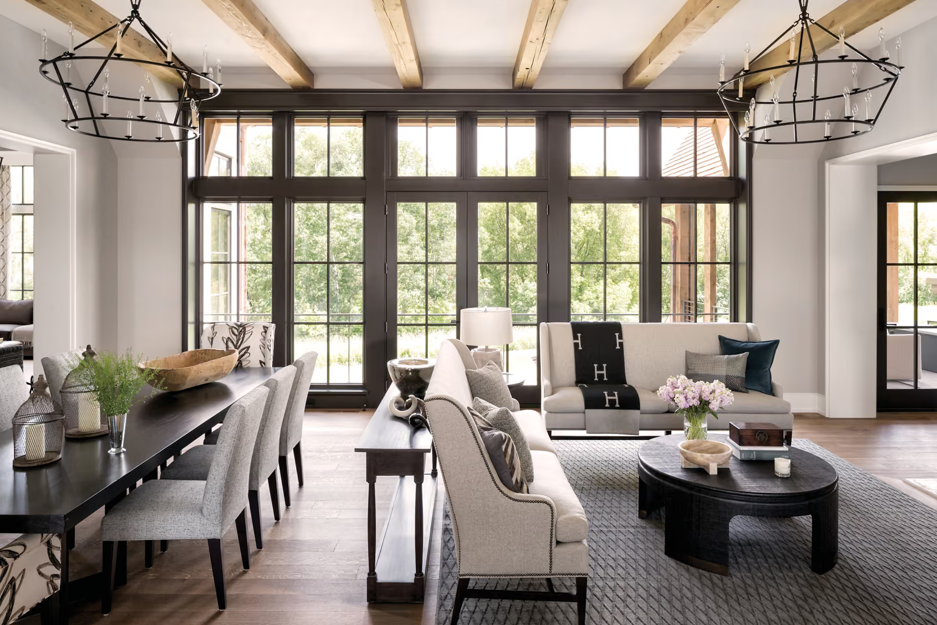 Bright modern living room with large windows, neutral furniture, and rustic wood beams