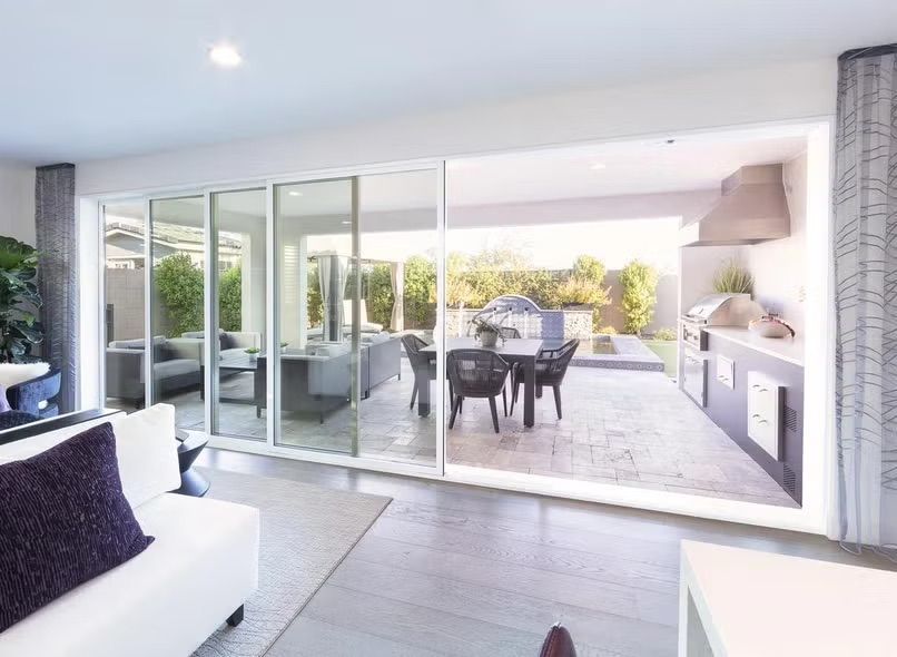 Modern patio view from a bright living room, with sliding glass doors, outdoor dining table, and kitchen area