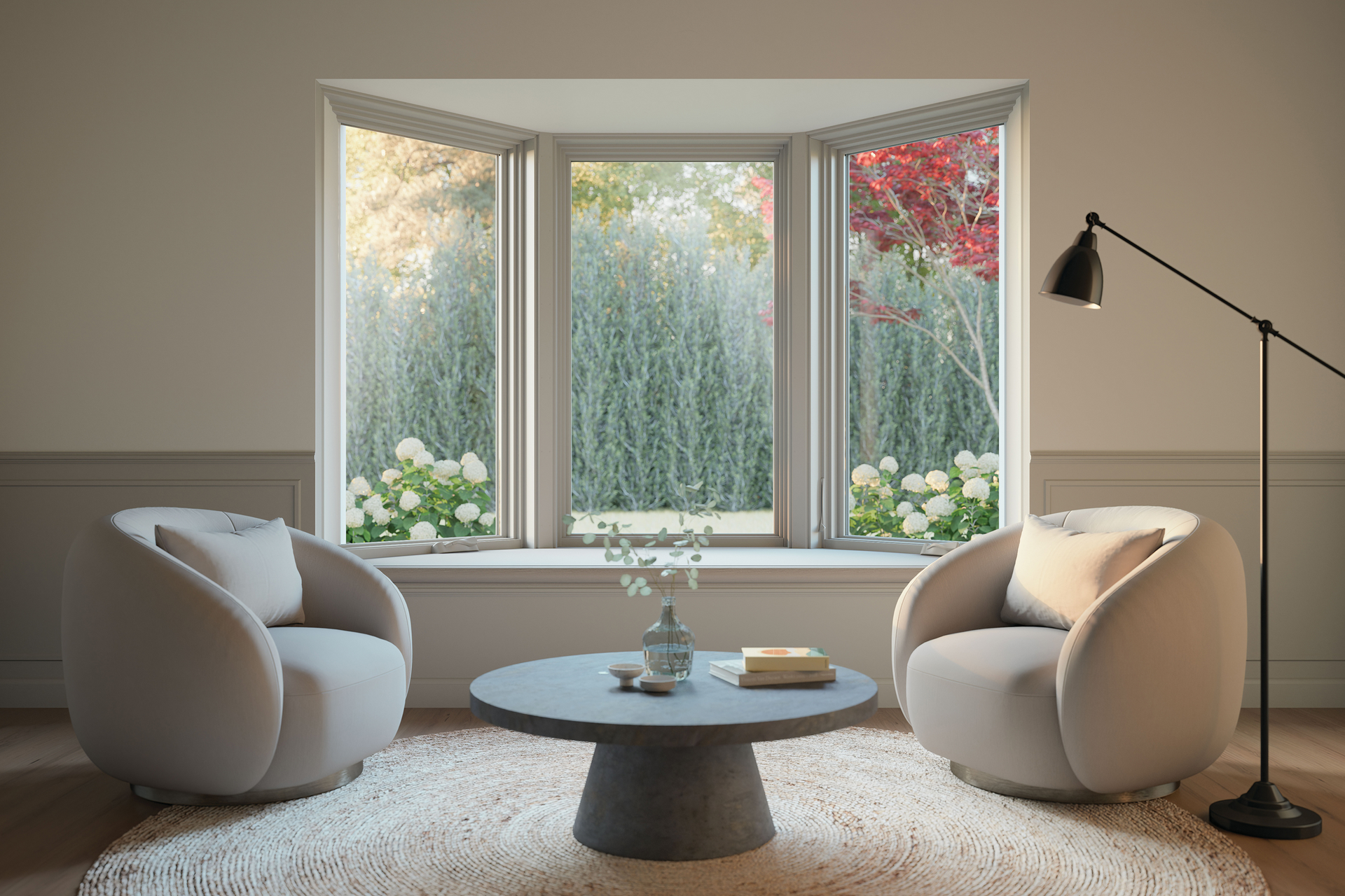 Cozy modern living room with two cream chairs, round table, floor lamp, and bay window overlooking greenery.