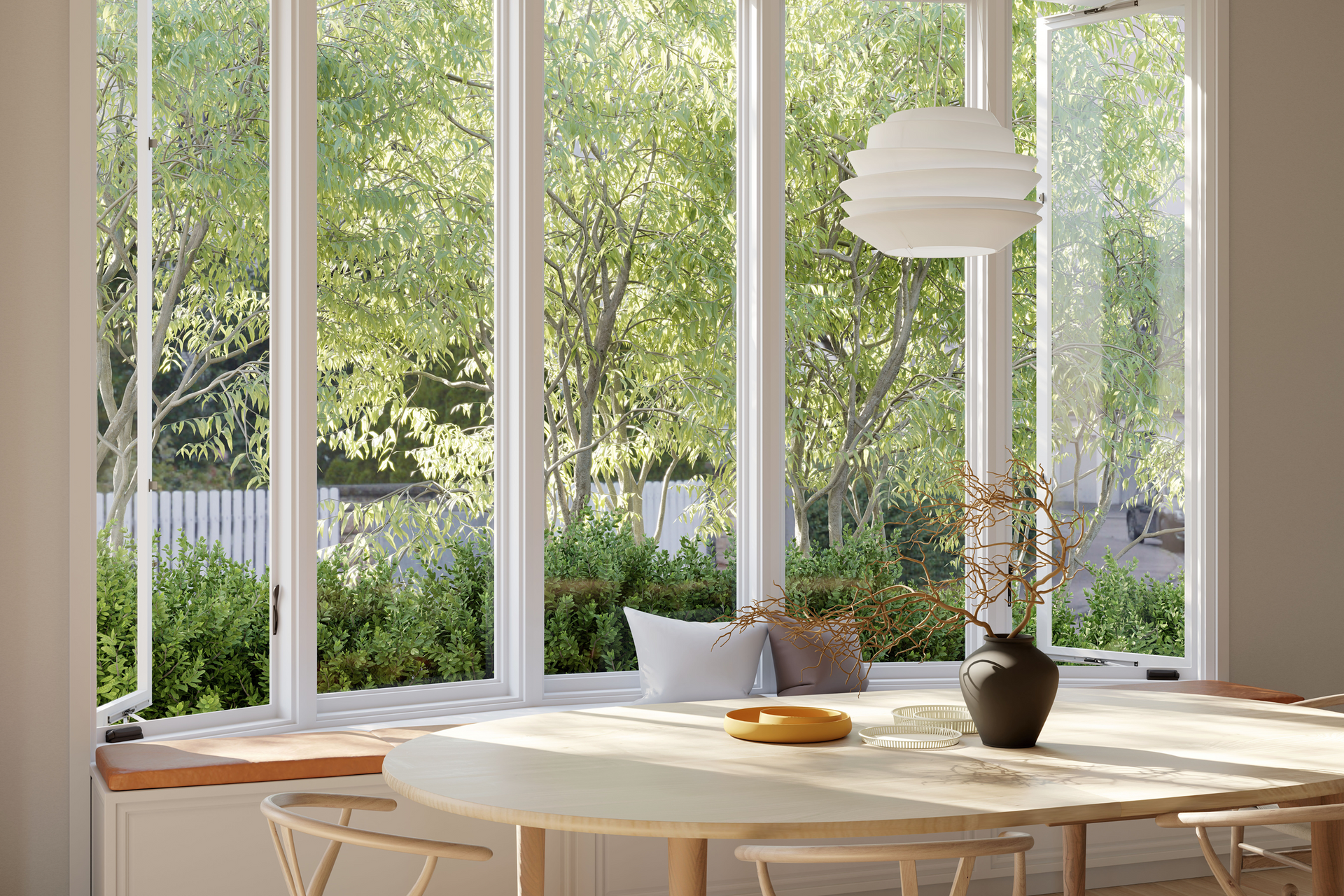 Bright sunlit dining room with large windows, round wooden table, and green garden view outside