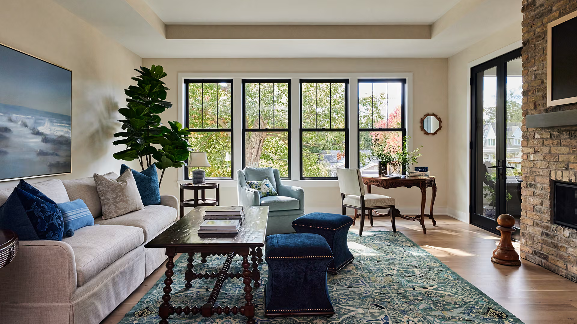 Modern living room with gray sofa, blue chairs, large windows, fireplace, and patterned rug
