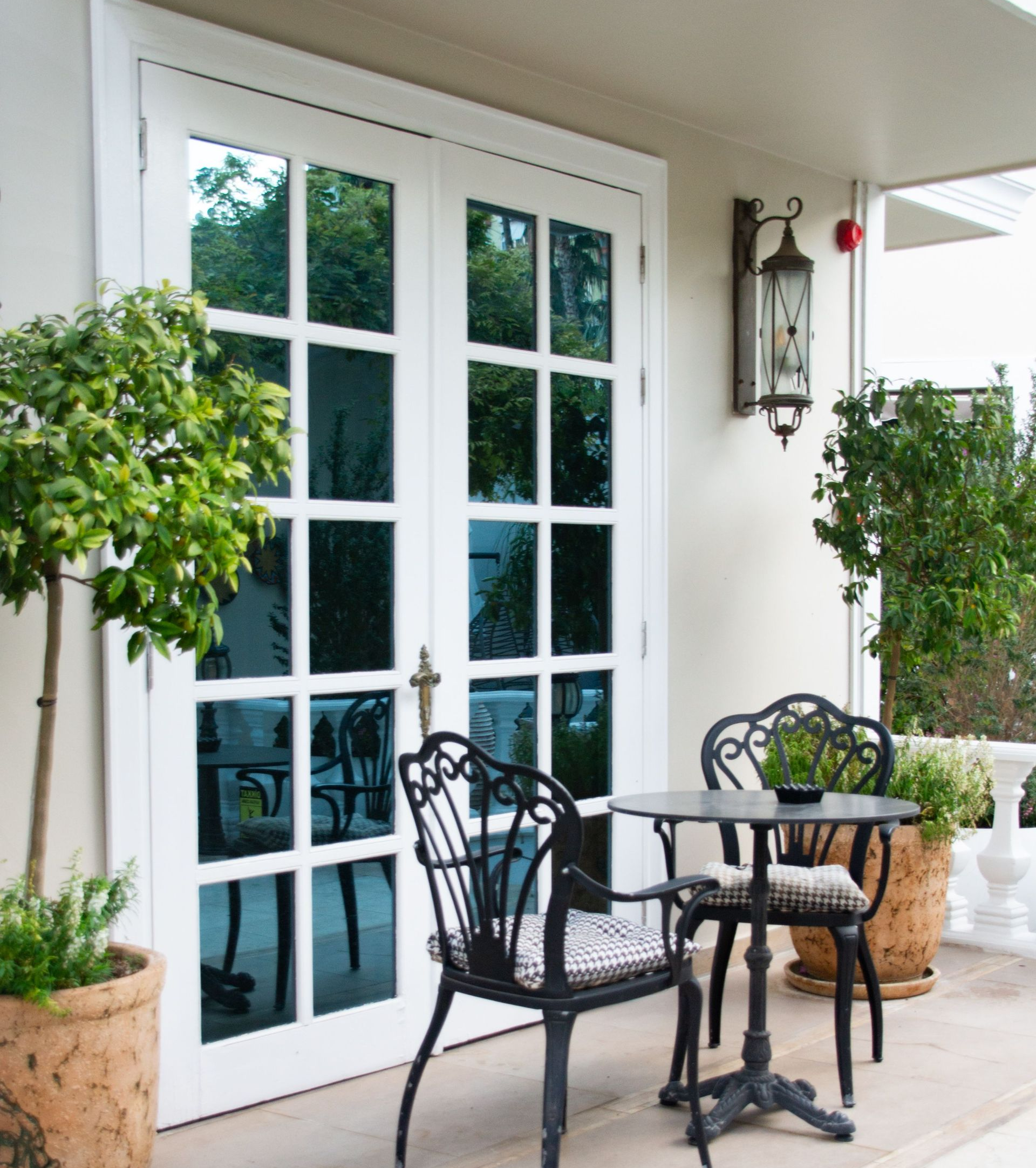 White French doors beside a small black patio table and chairs on a covered porch with potted plants