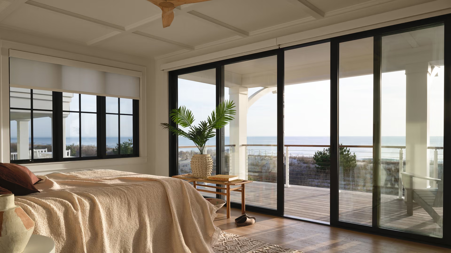 Bright bedroom with large glass doors opening to a sunlit patio and ocean view