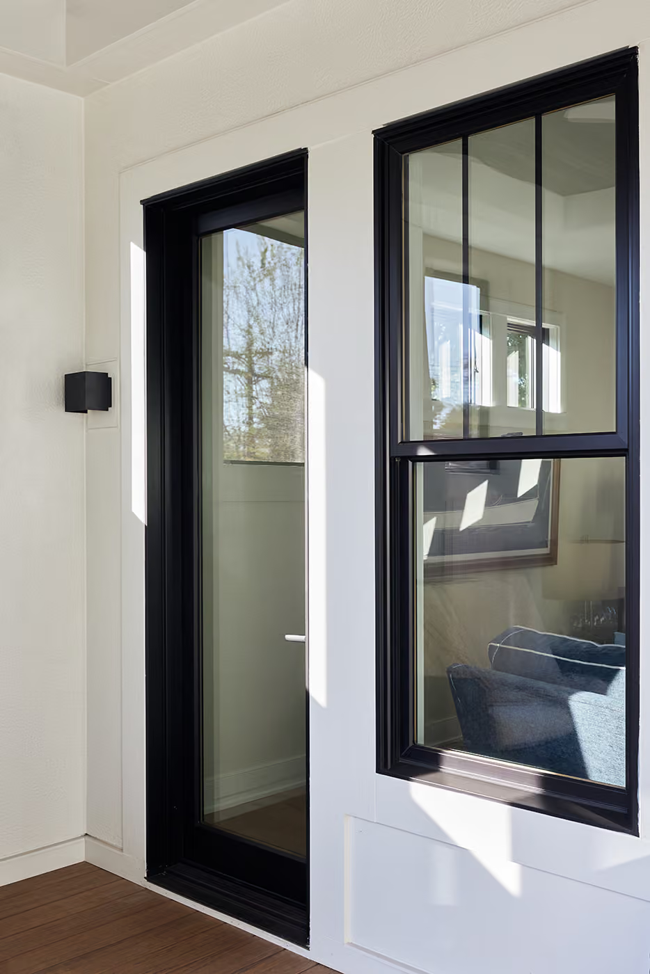 Black-framed door and window on a white exterior wall with a small wall light and wooden deck.
