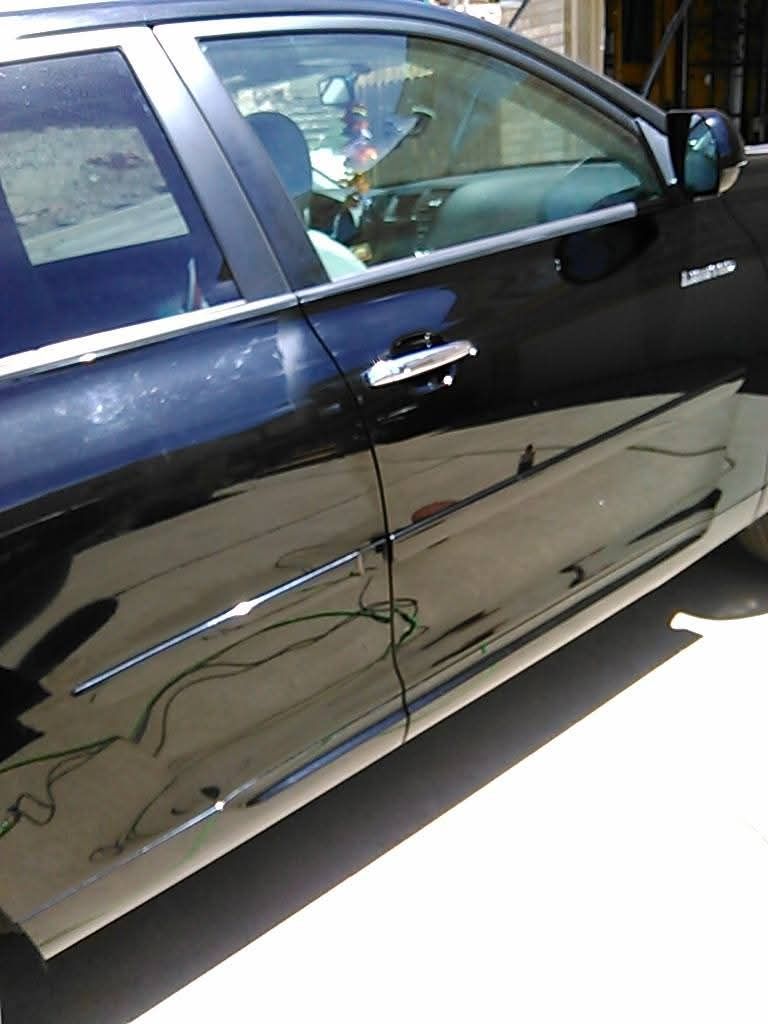 Close-up view of the side of a shiny black car, showing the doors, handle, and a partial reflection of the surroundings.