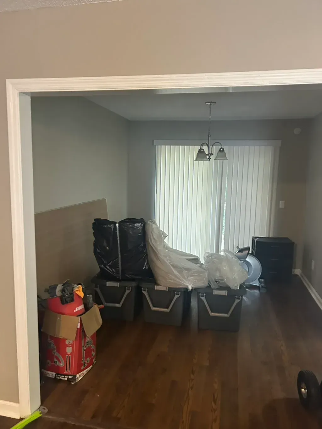 An open doorway reveals a room with dark wood floors, three storage bins, packed items, and a glass sliding door.