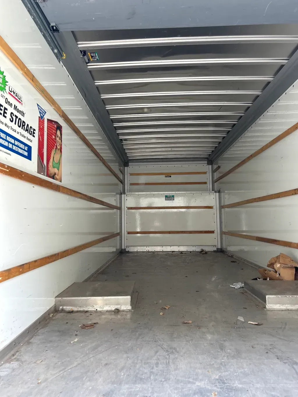 The interior of an empty, clean moving truck with white walls, wooden cargo tracks, and a metal floor.