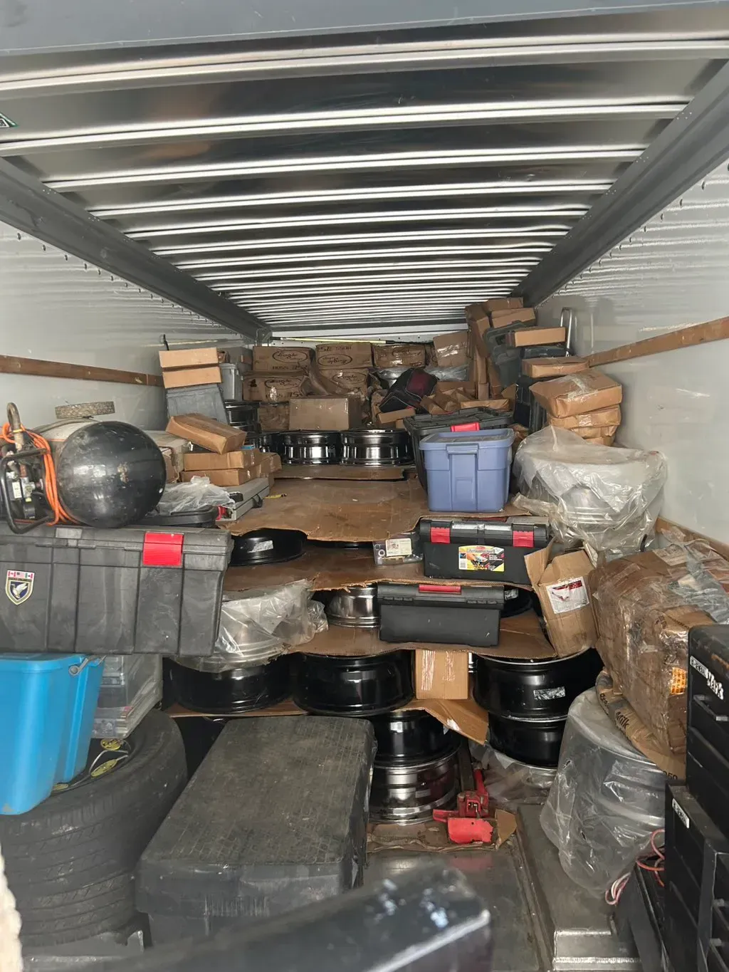 Interior of a moving truck packed with various boxes, plastic storage bins, equipment cases, and several vehicle tires.
