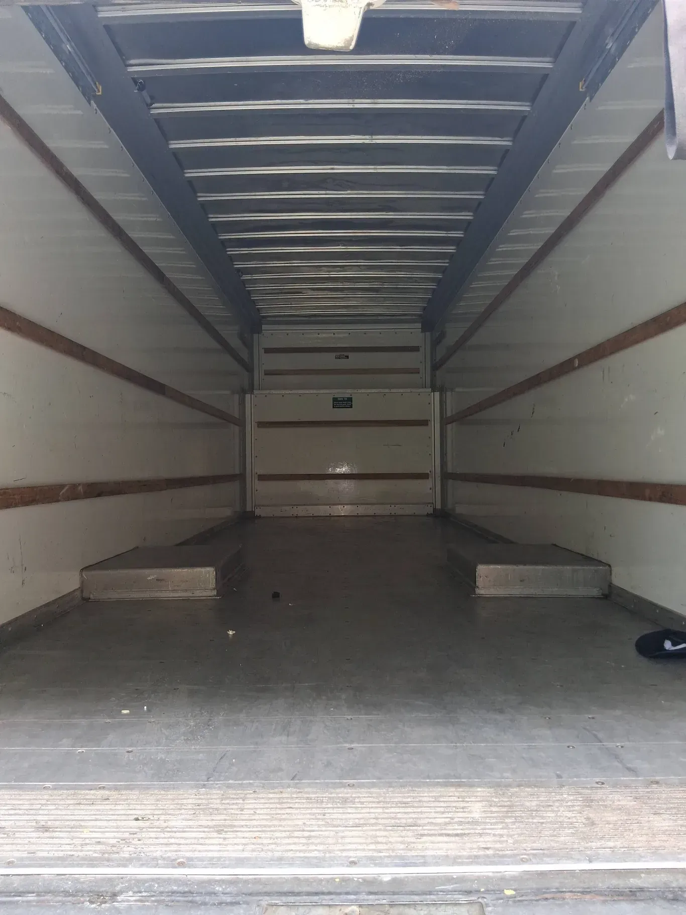 The interior of an empty, rectangular box truck with light-colored walls and metal floor rails.