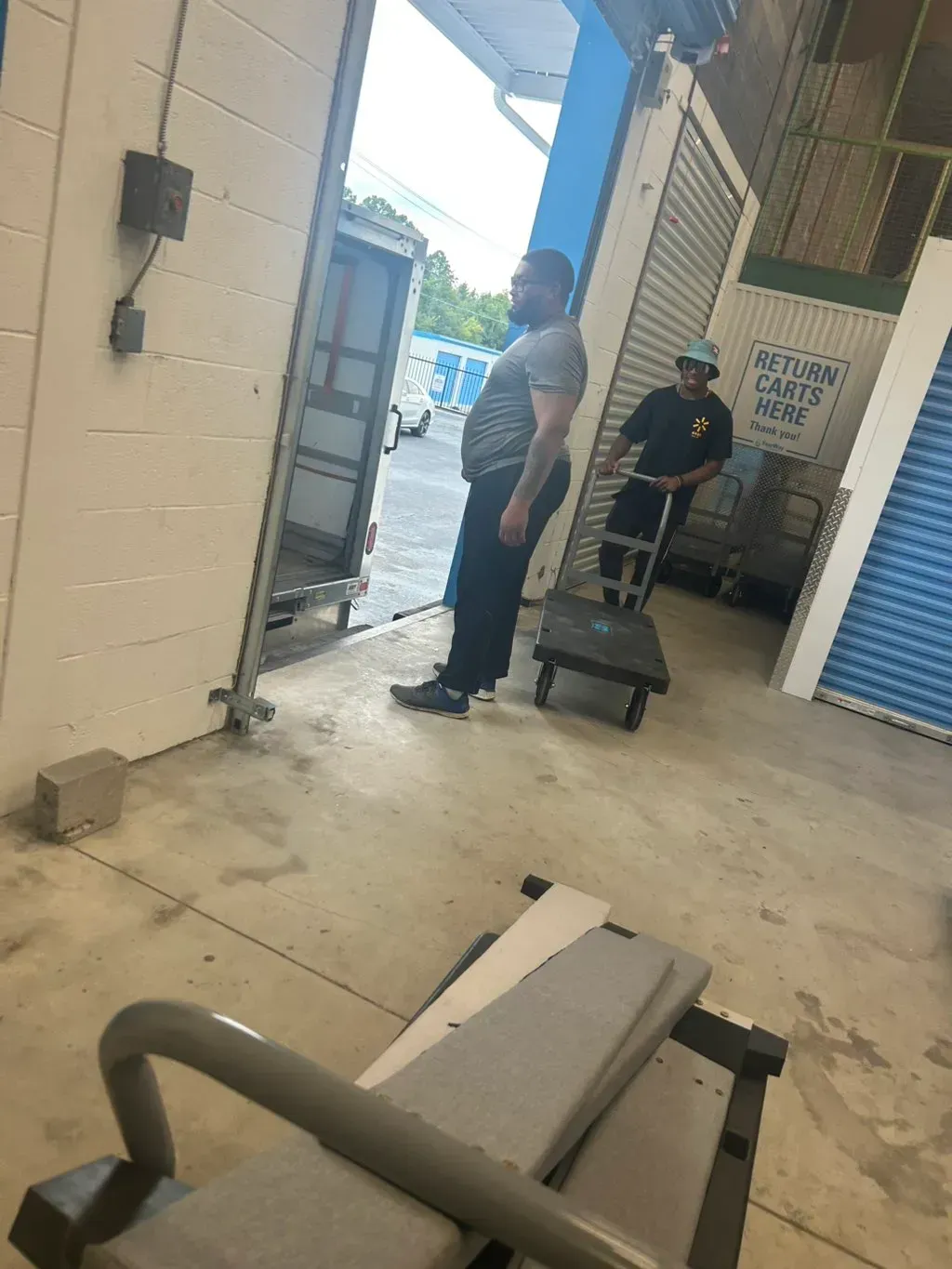 Two people maneuver a cart through an open warehouse bay door.