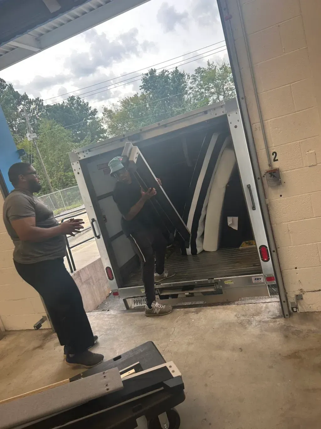Two people loading or unloading large pieces of furniture from the back of a truck in an industrial loading bay.