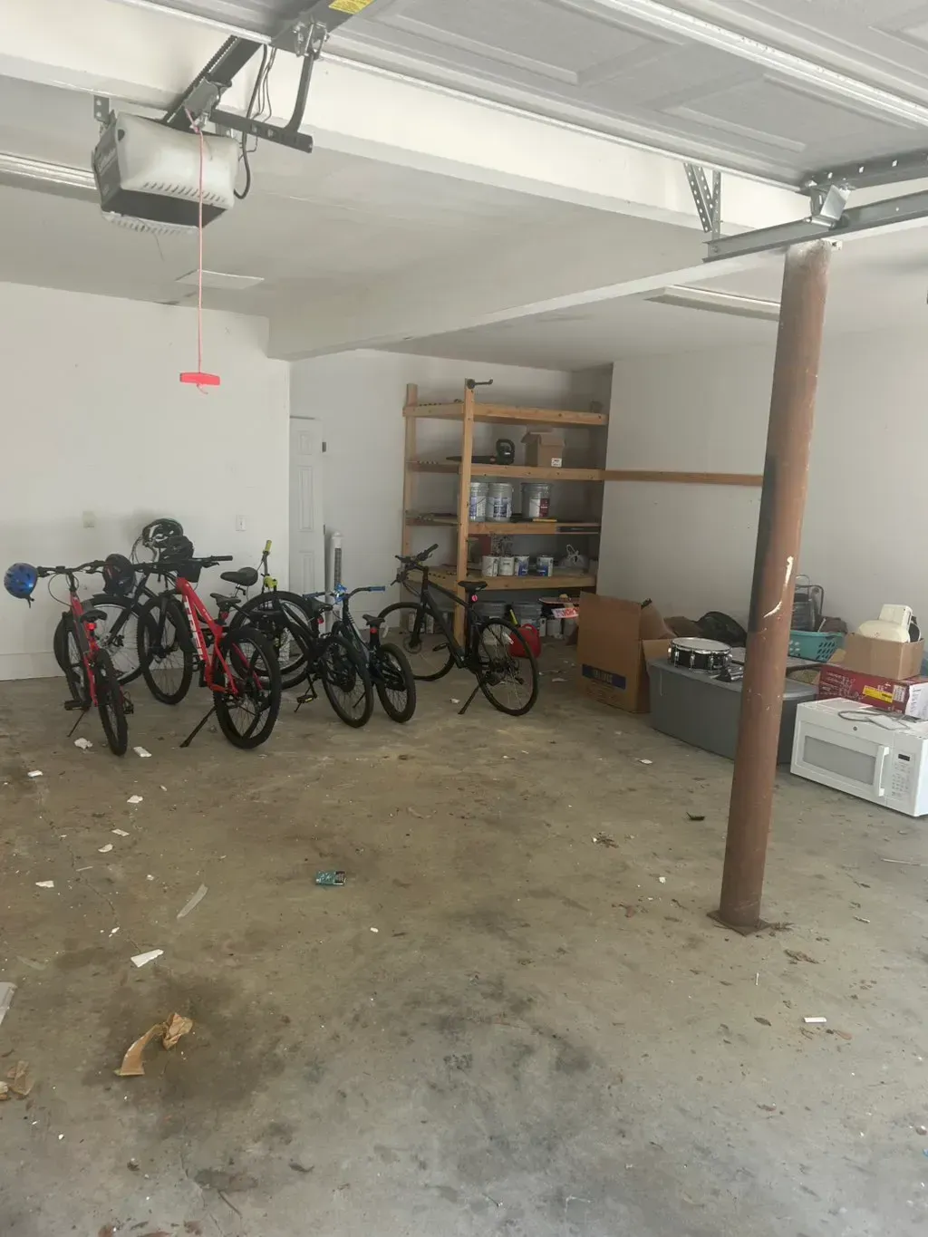 A cluttered residential garage featuring several bicycles, wooden storage shelving, and a metal support pole.