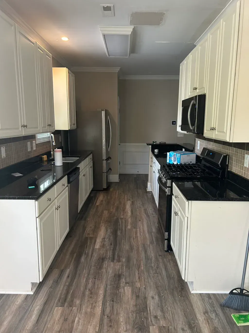 A kitchen with white cabinets, black countertops, stainless steel appliances, and wood-look flooring.
