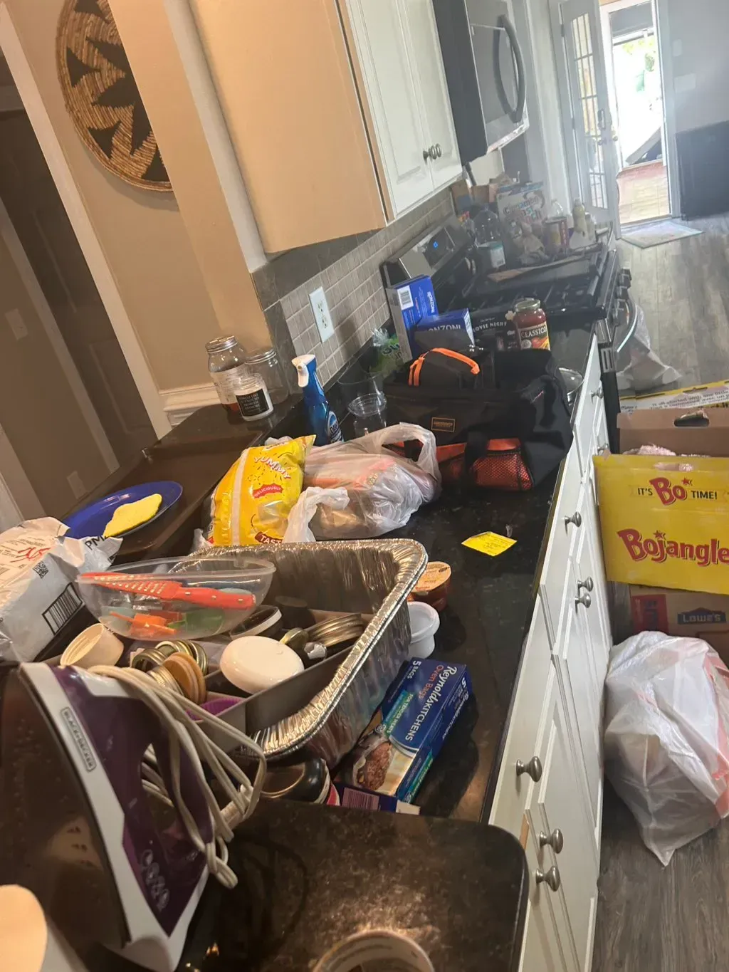 A cluttered kitchen counter with a food box, groceries, a disposable roasting pan, and a clothes iron.