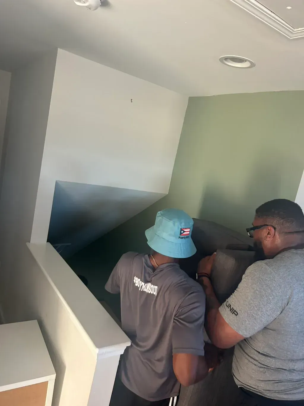 Two individuals in casual attire lift and move a piece of furniture into an open space in a home.
