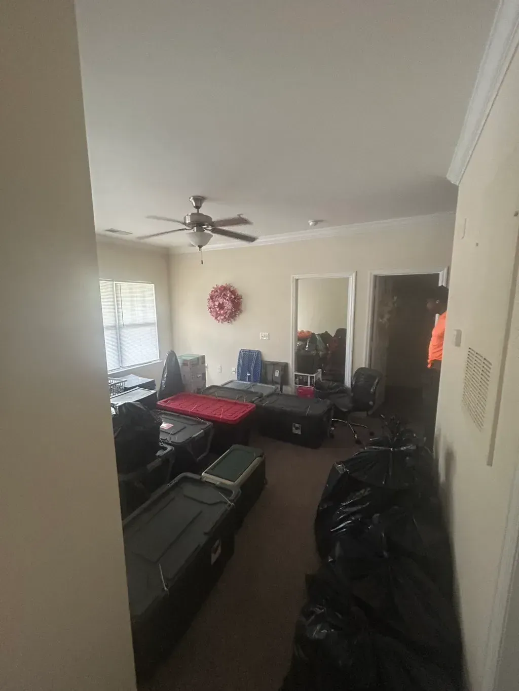 A room filled with black storage totes, black trash bags, and a red mat, seen from a doorway.