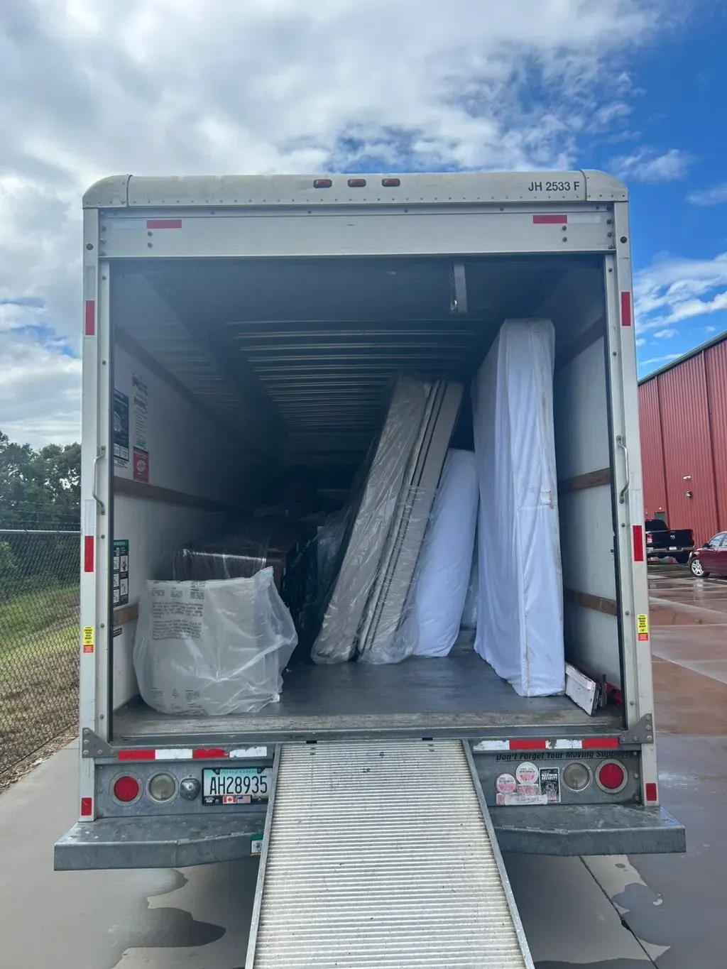 The rear view of a box truck parked outdoors, showing its open interior filled with large furniture items in protective wrap.