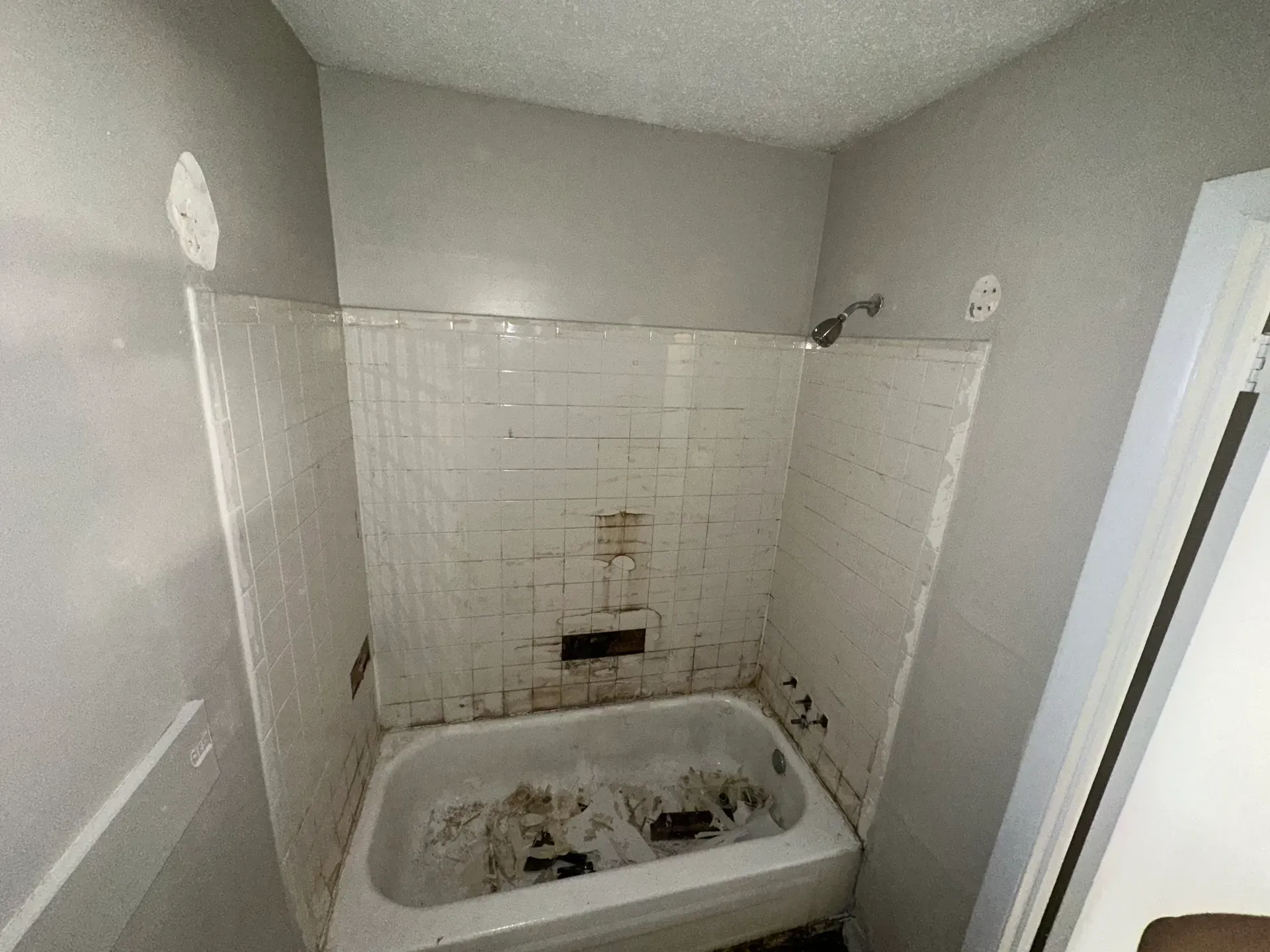 A white bathtub in a tiled alcove, with missing shower fixtures and unfinished walls in a bathroom.