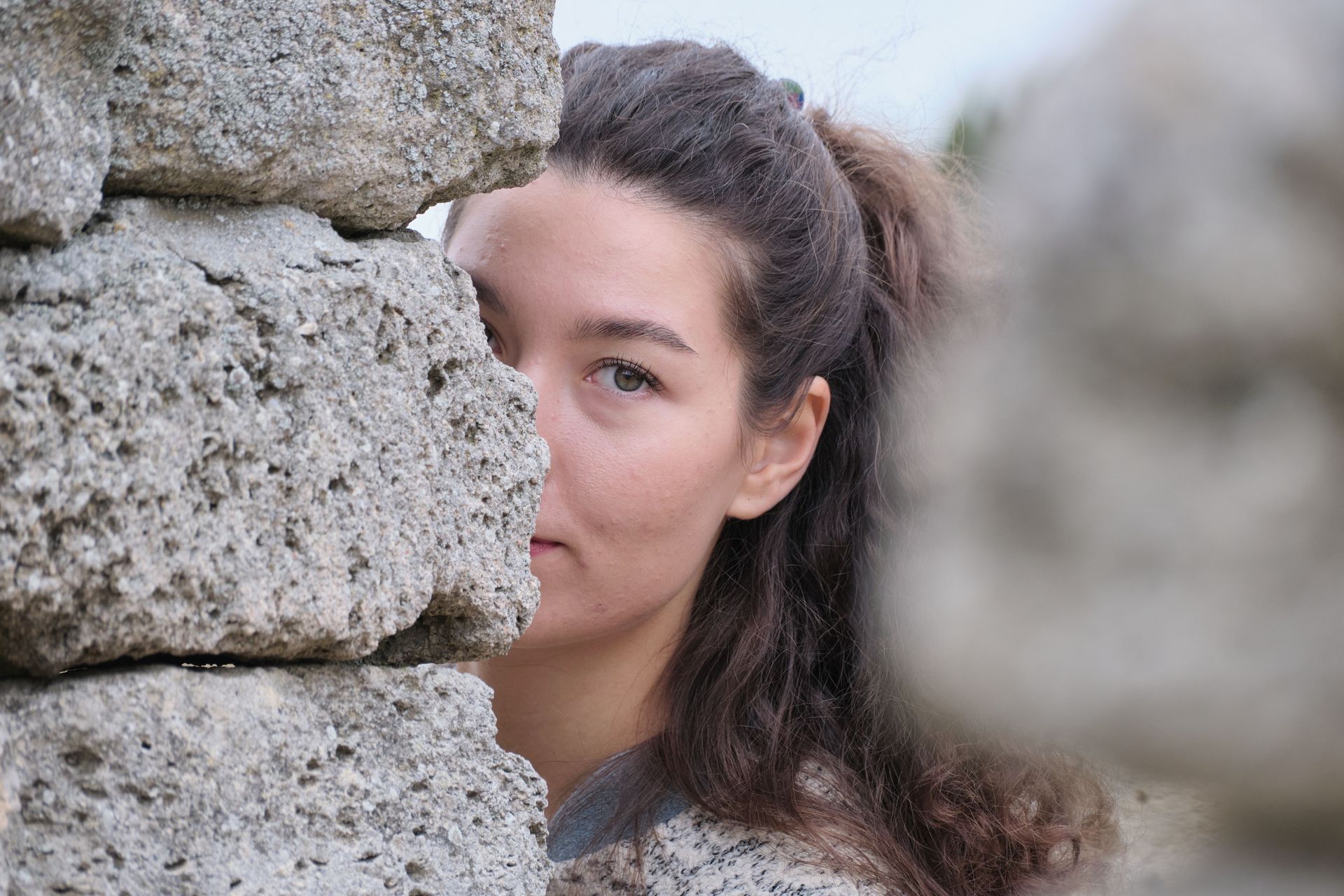 woman hiding part of her face beind a stone wall