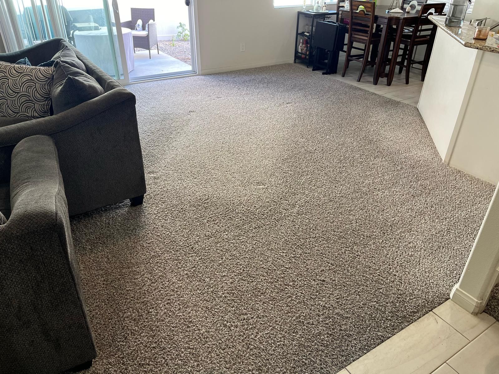 Carpeted living room with couch, open doorway to patio, and dining table in the background