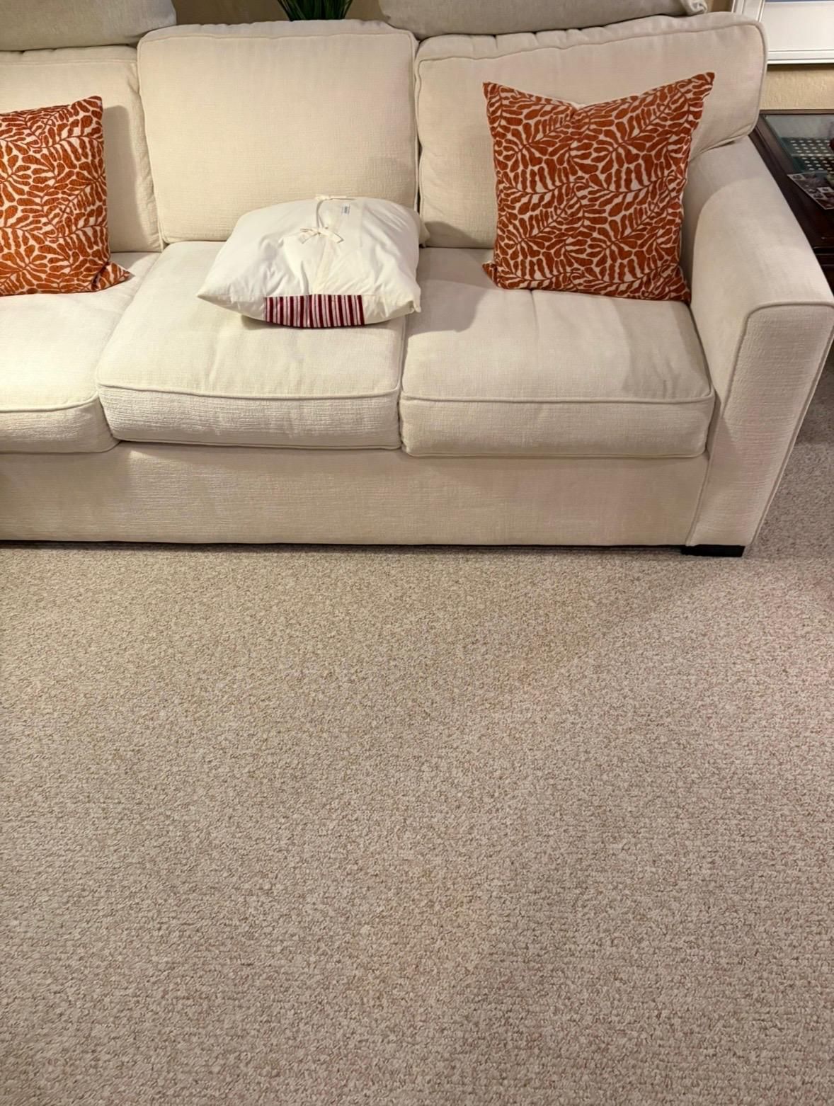 Beige sofa with orange and white pillows on a light carpet in a living room.