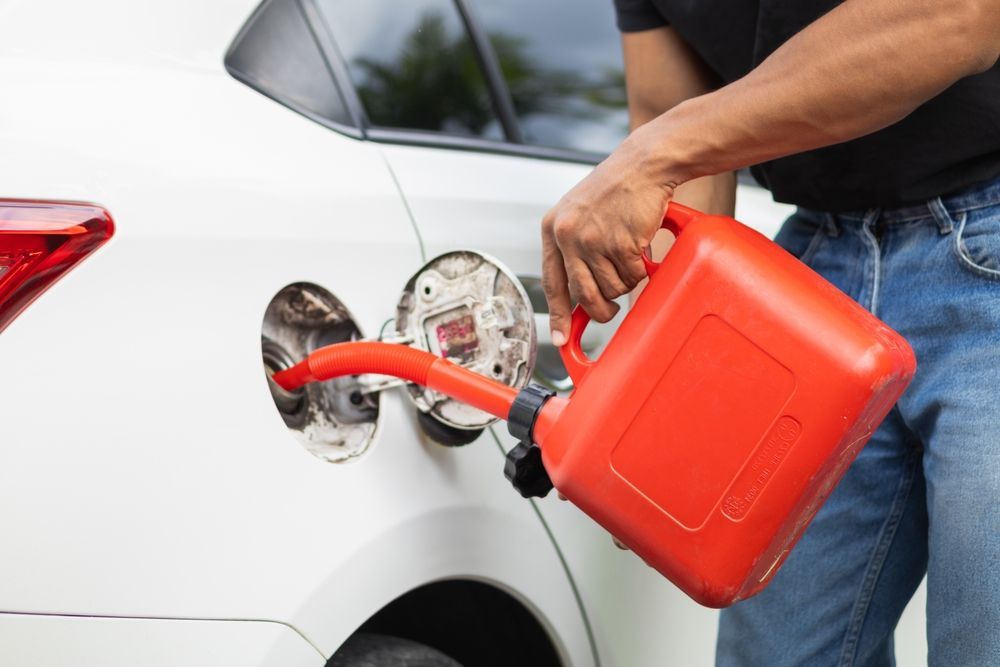 Person refueling a white car with a red gas can at the fuel door