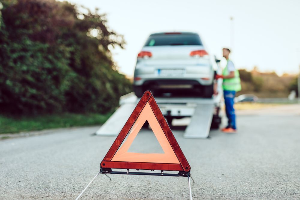 Red roadside warning triangle in front of a car on a tow truck, with a person standing nearby.