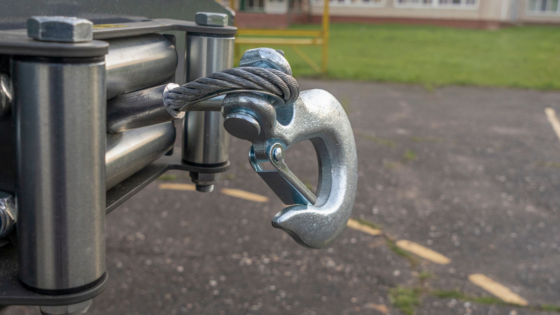 Metal gate latch with a silver hook and rope on a paved outdoor path