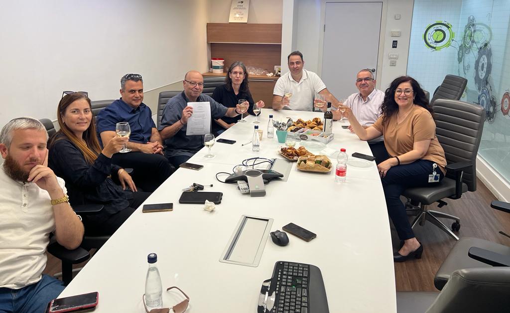 קבוצת אנשים יושבת סביב שולחן ארוך בחדר ישיבות.