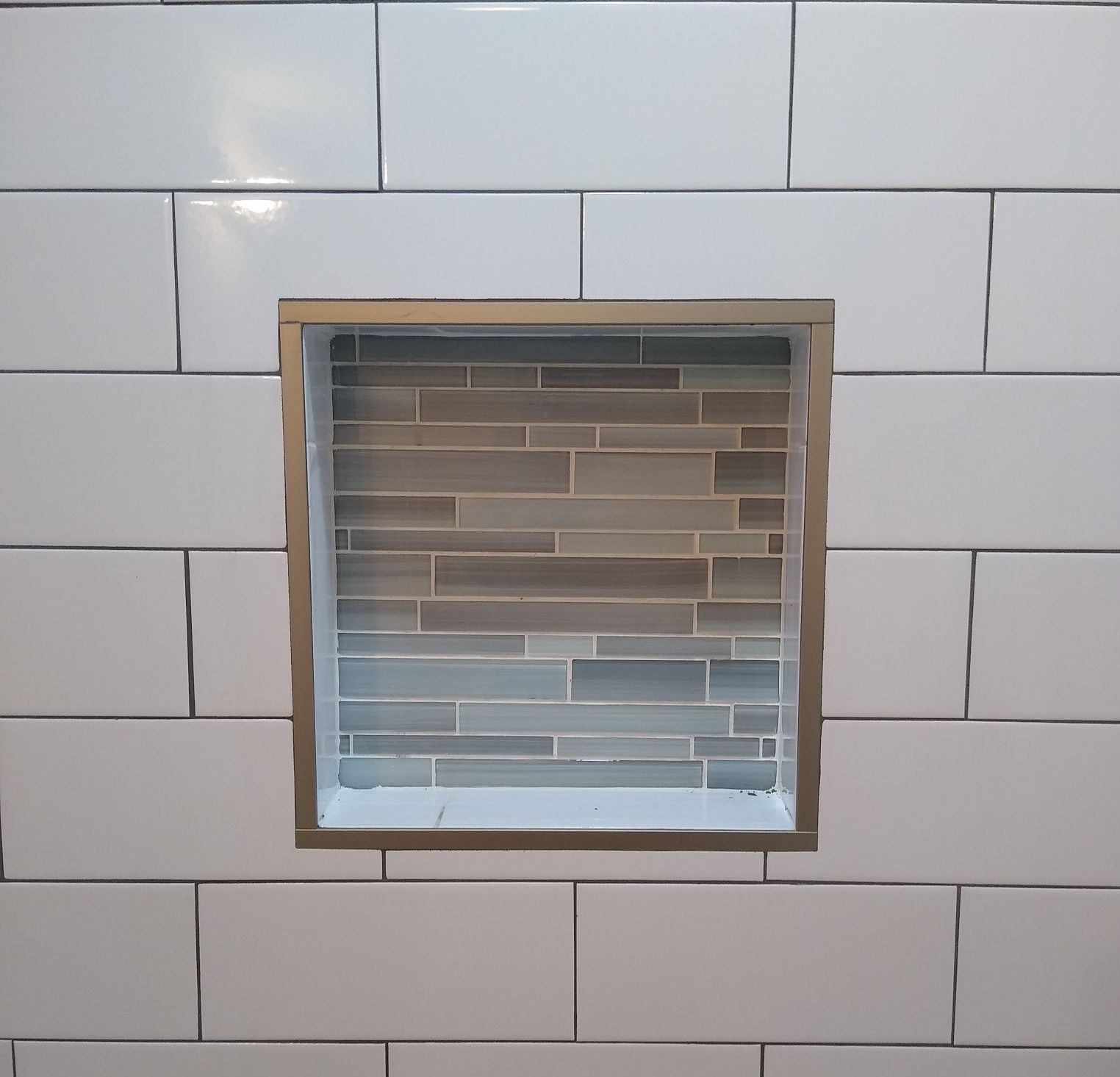 A white tiled wall with a niche in the middle of it.