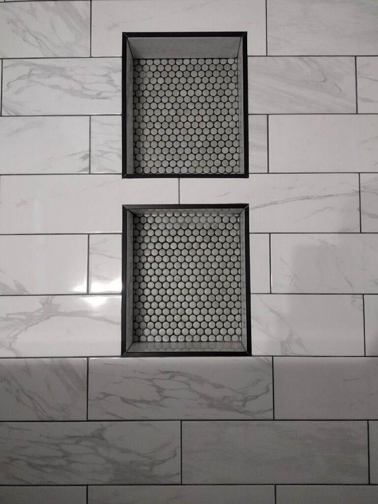 A bathroom wall with white tiles and a shower niche.