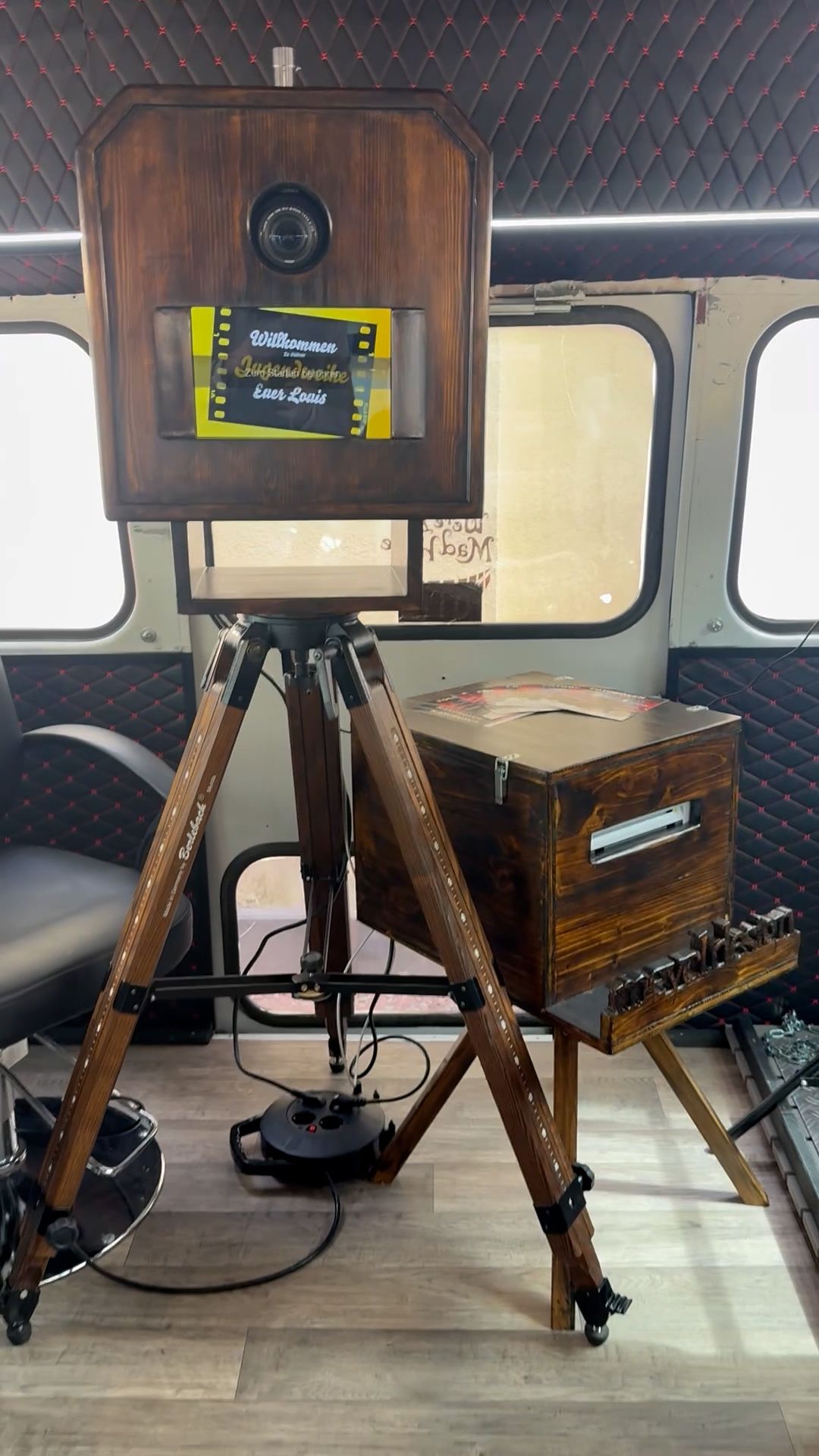 Fotoautomat aus Holz mit angebrachtem Licht, auf einem Stativ montiert.