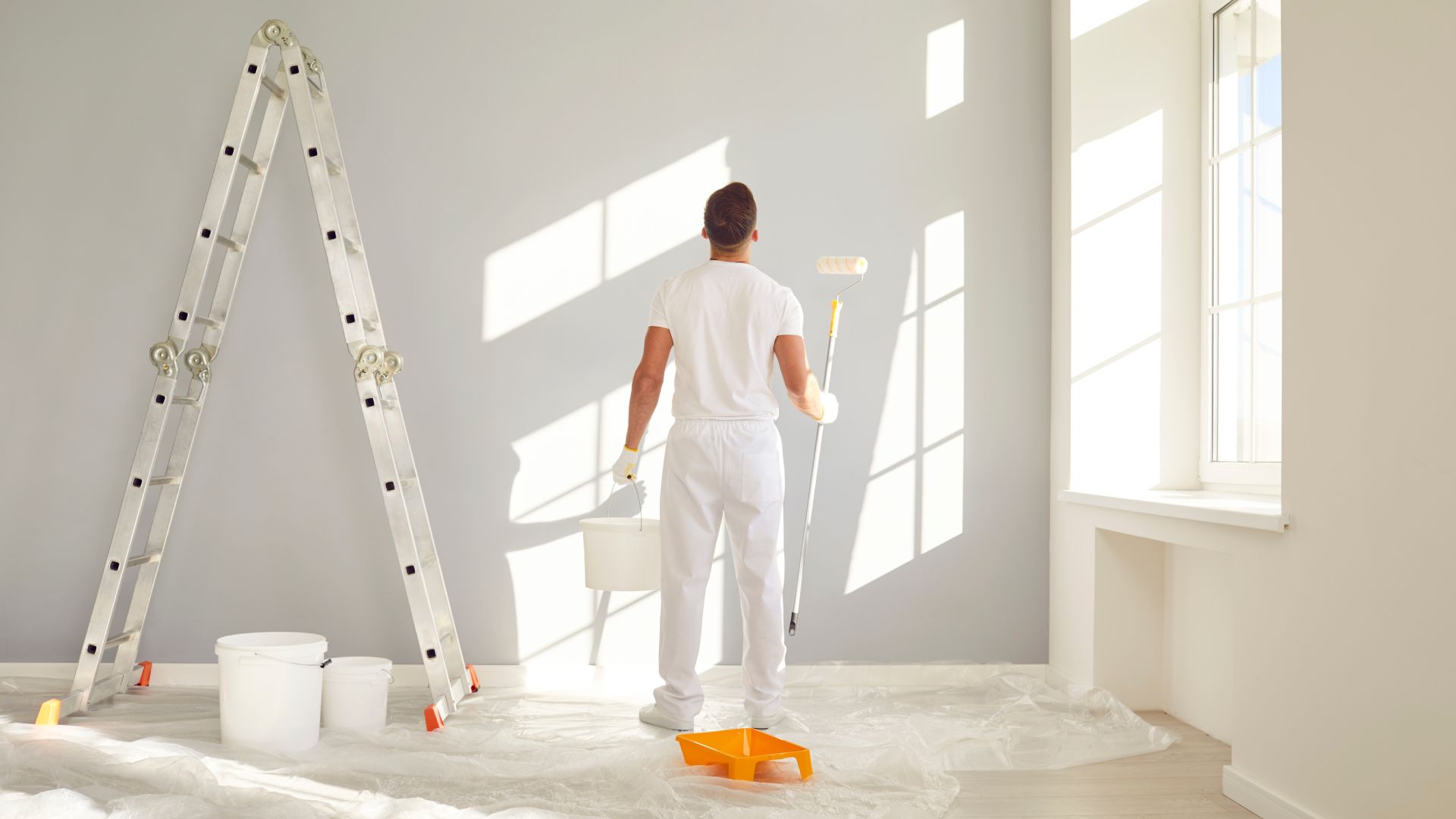 A man is painting a wall in an empty room.
