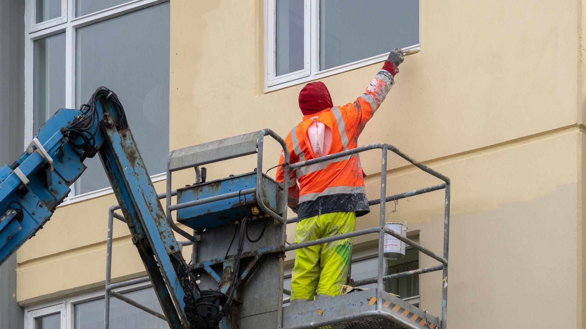 A man is painting a building from a crane.