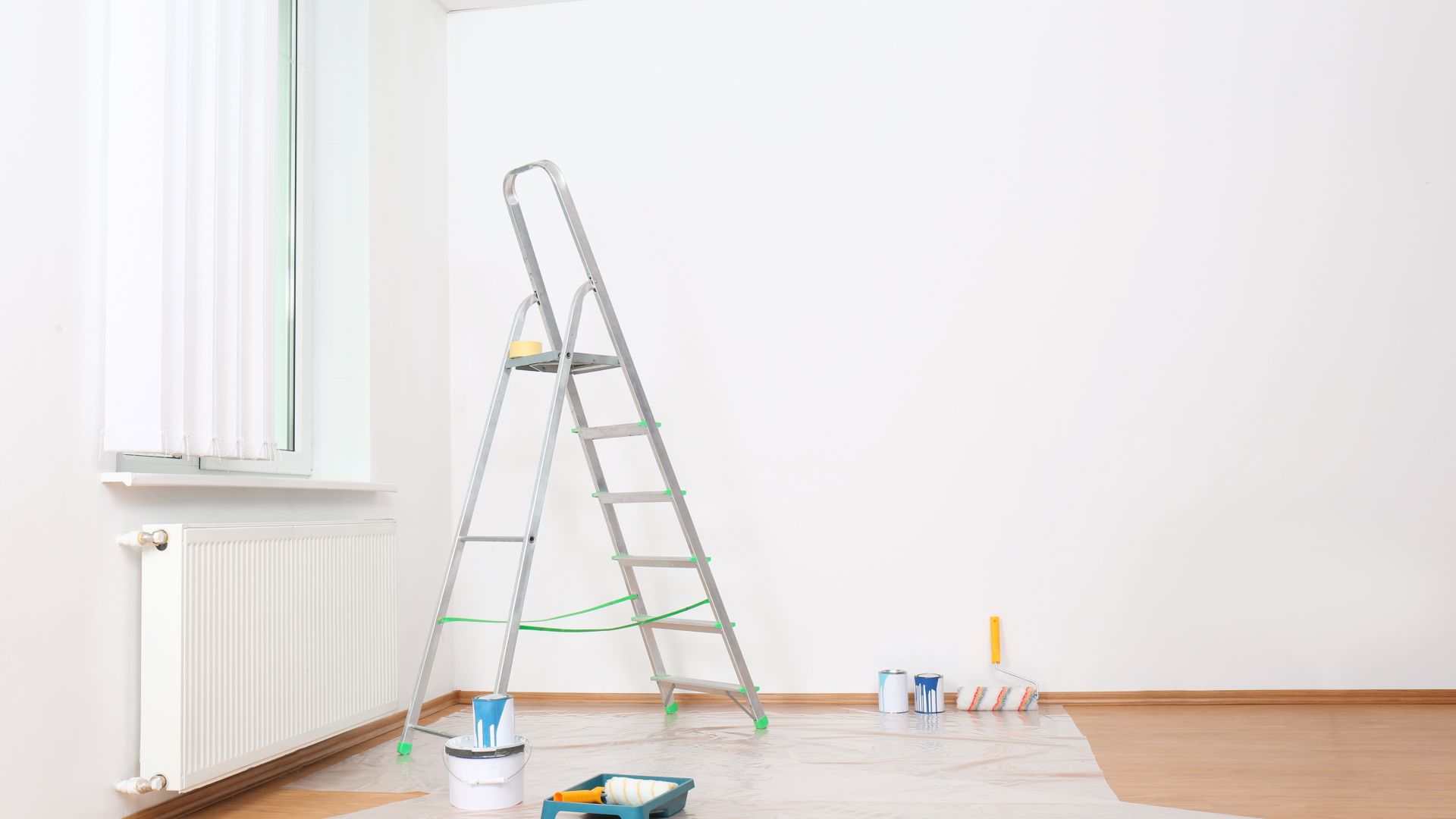 An empty room with a ladder , paint buckets and brushes.