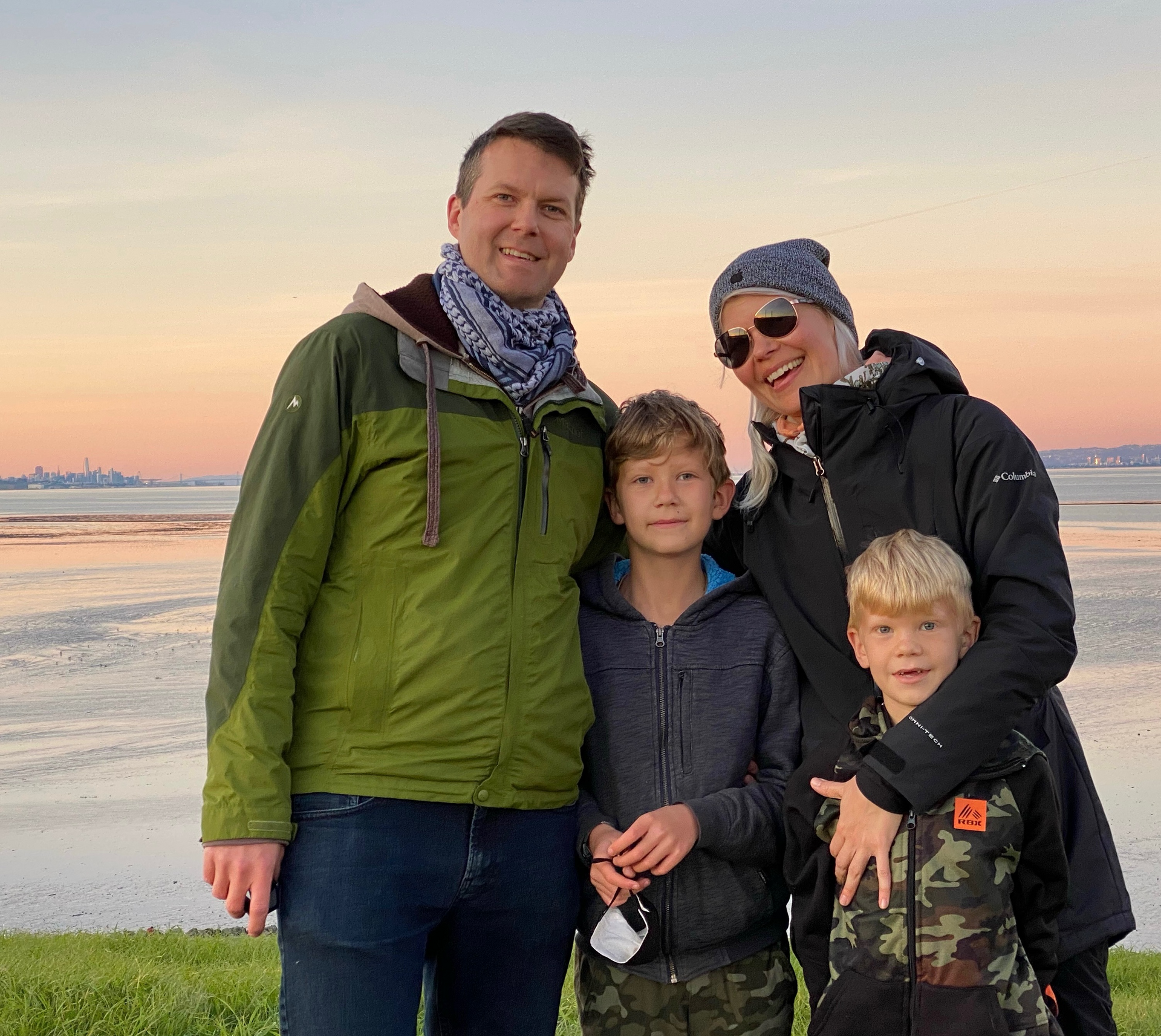Family of four smiling at sunset with San Francisco skyline in the background.