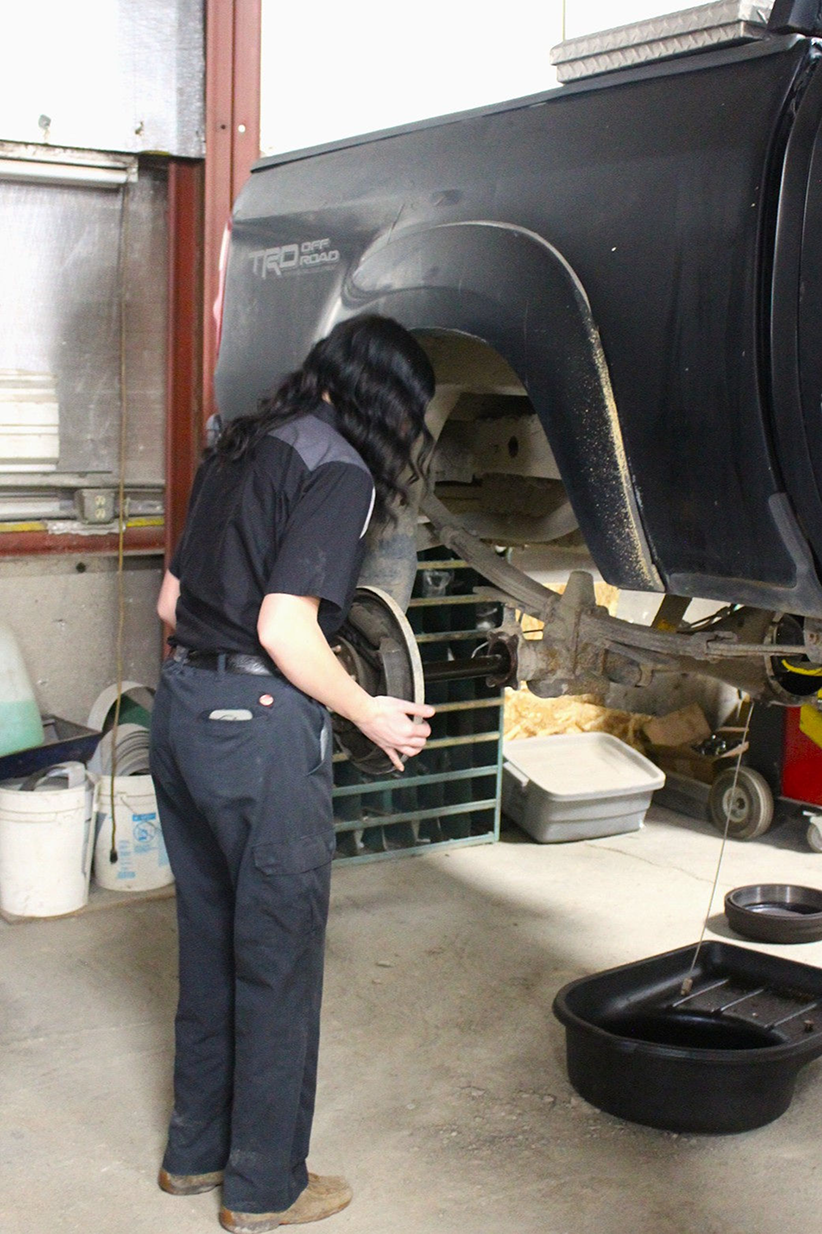 Person in work clothes removing a brake drum from a black truck in a garage | Don's Repair