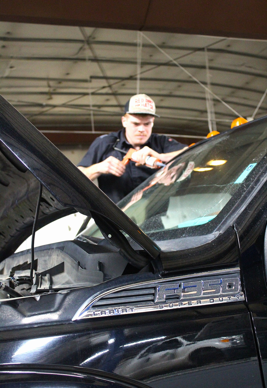 Mechanic working on a black truck with the hood open, inside a garage | Don's Repair