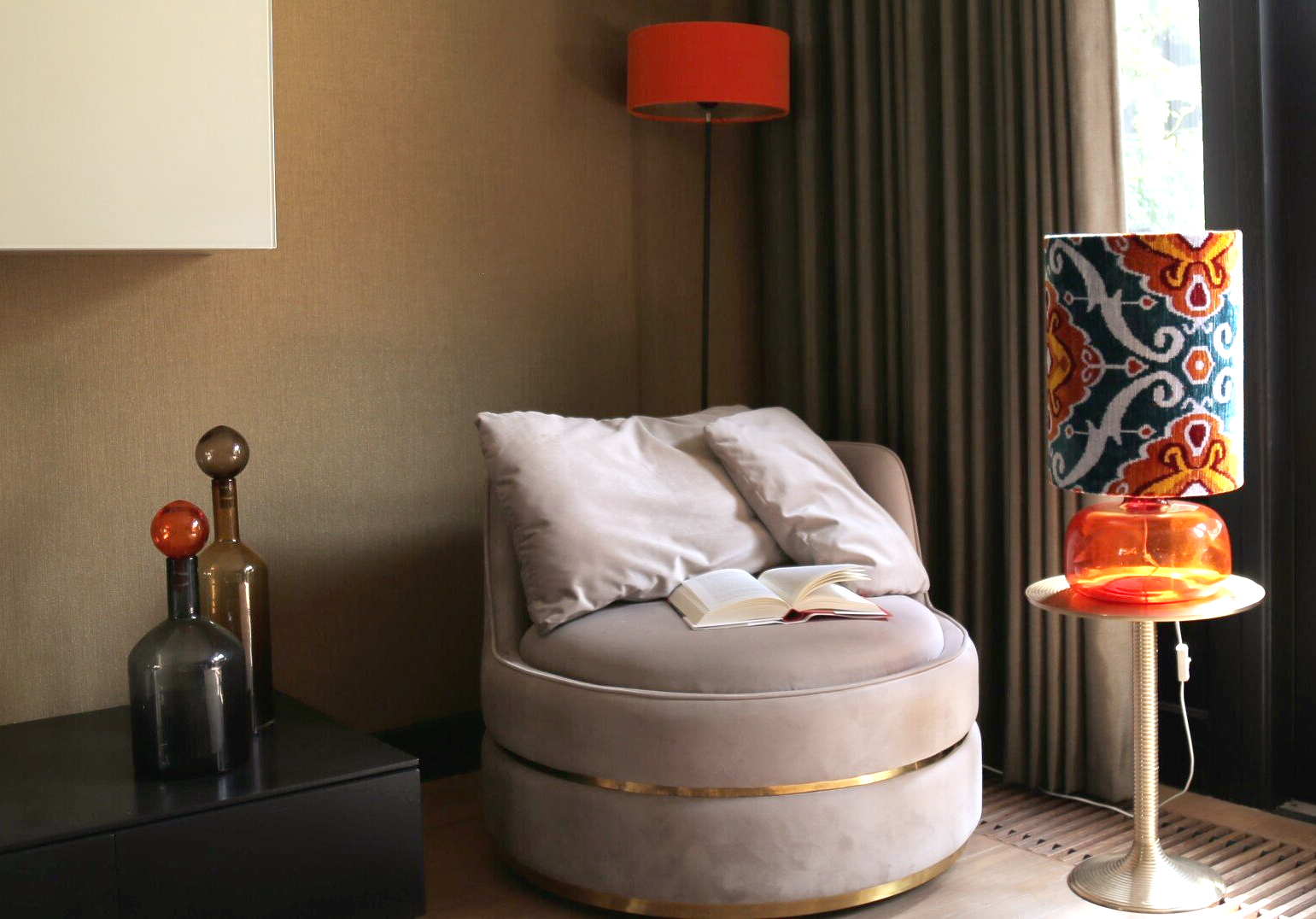 Een gezellig leeshoekje met een comfortabele stoel, een lamp met patroon en oranje accenten.