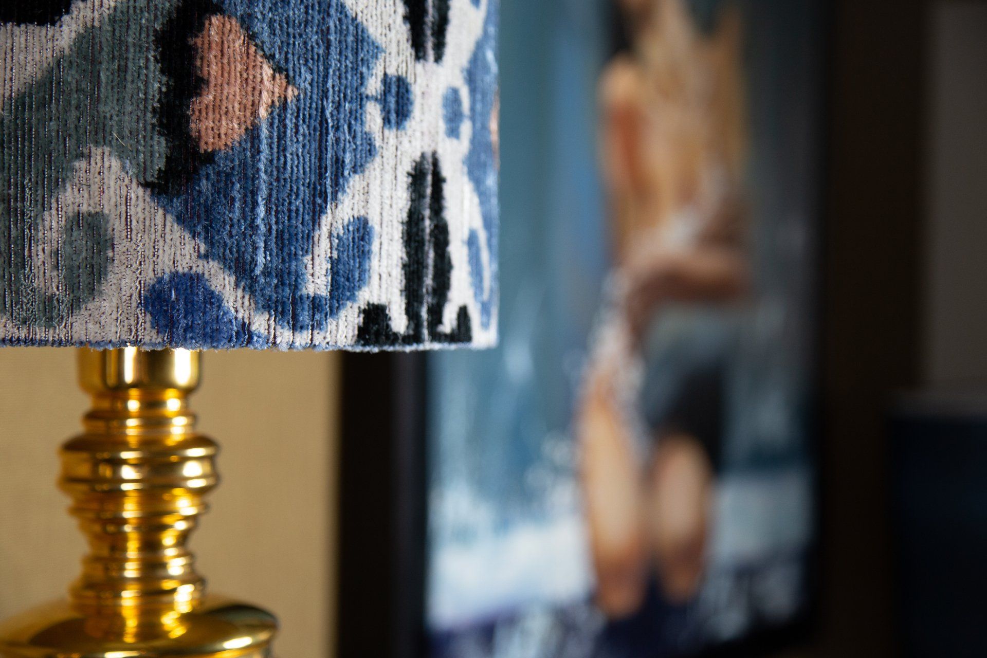 Gouden lampvoet met een blauw-witte lampenkap met patroon; wazige achtergrond van een persoon.