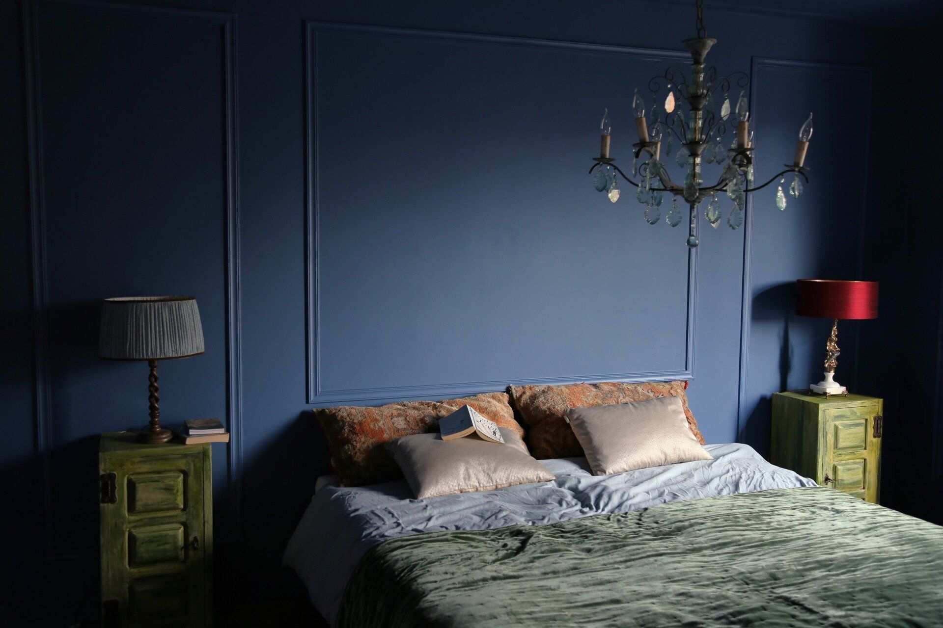 Blauwe slaapkamer met bed, nachtkastjes, kroonluchter en lampen.