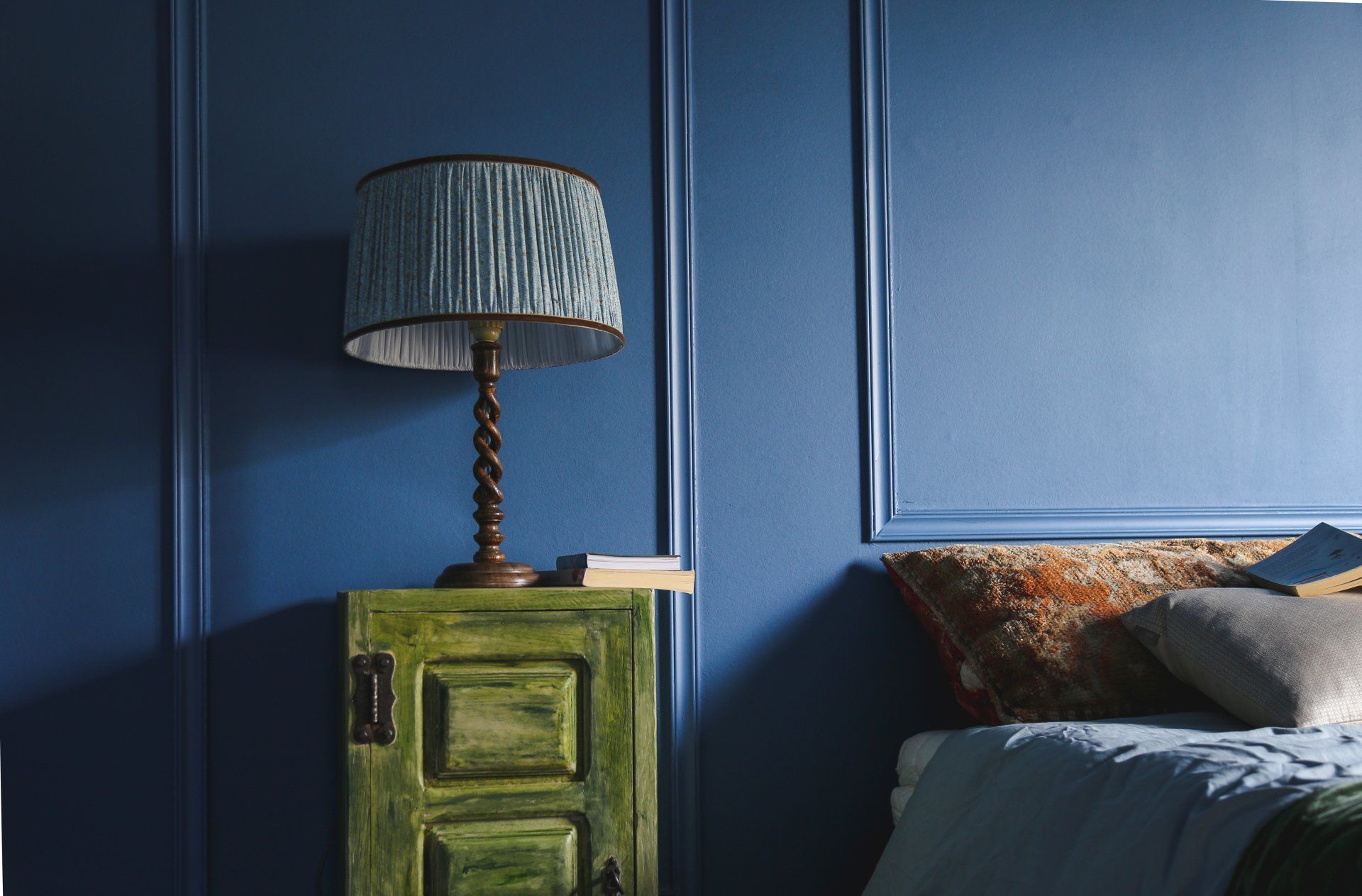Blauwe slaapkamer met groene kast, lamp en bed met kussens.